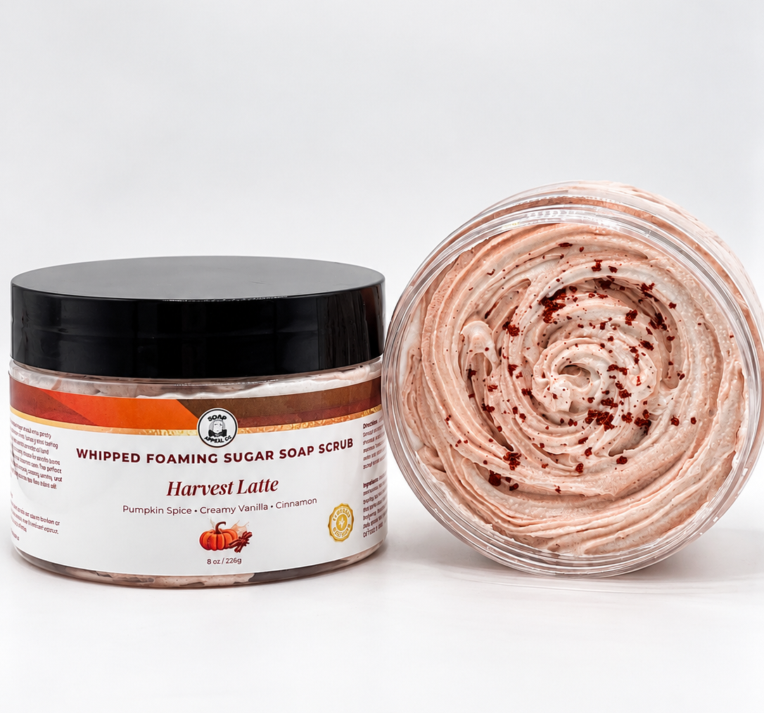 A jar of whipped foaming sugar soap scrub labeled 'Harvest Latte' with a black lid, shown next to an open clear jar displaying the swirled pale pink scrub with dark red specks, on a white background.