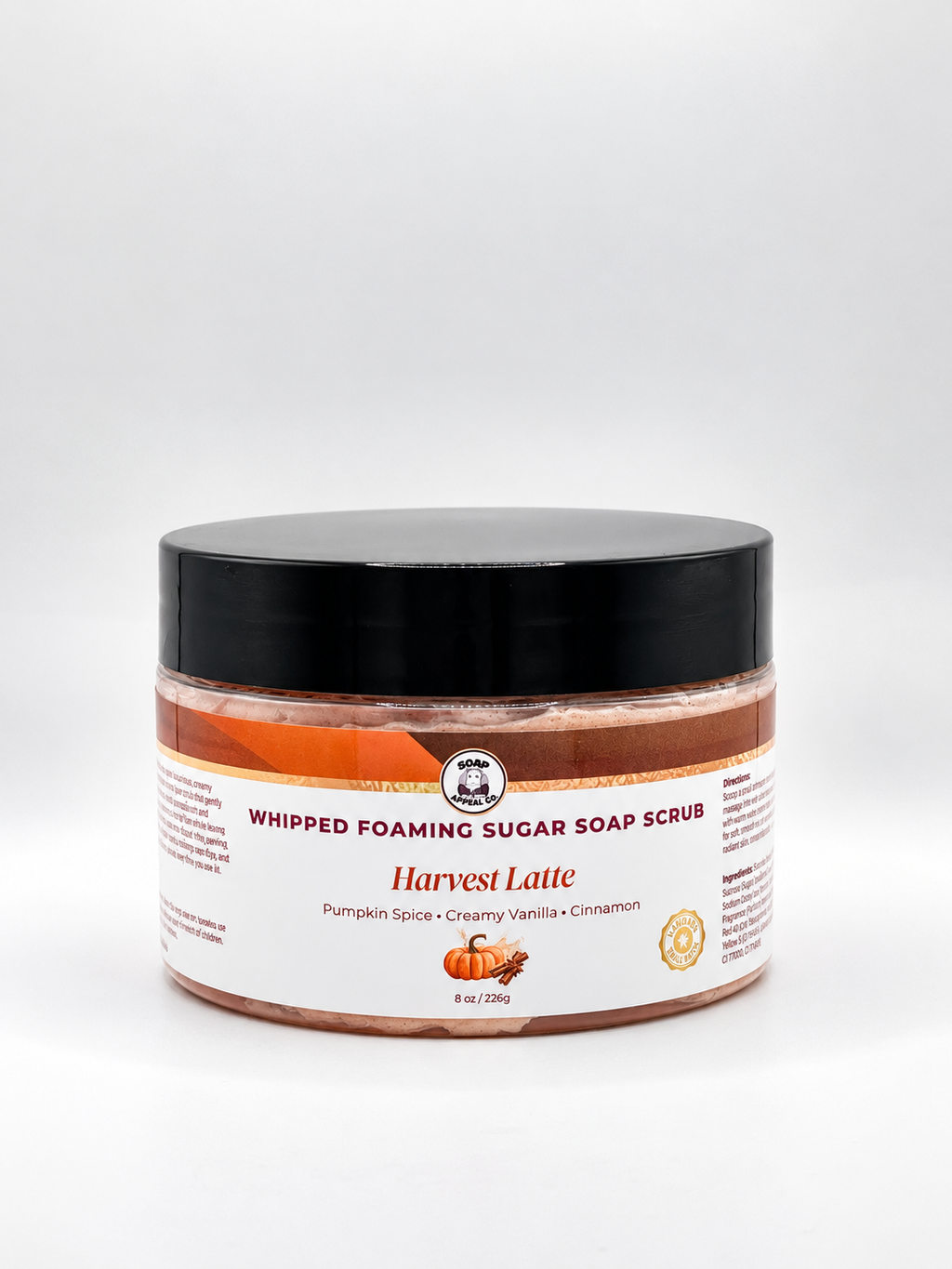 A jar of Whipped Foaming Sugar Soap Scrub in the Harvest Latte scent, featuring a black lid and a white label with orange and brown accents, set against a plain light gray background.
