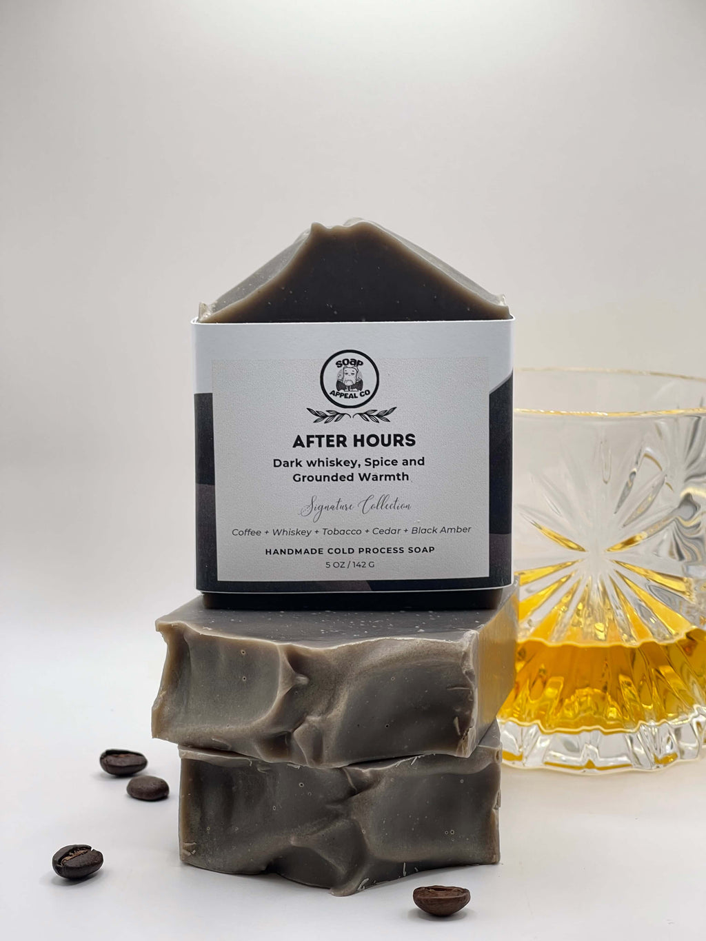 Bar of soap with a label titled 'After Hours' next to a glass of whiskey on a white background
