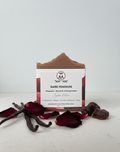 Bar of soap with a label on a white background, surrounded by vanilla beans and rose petals.