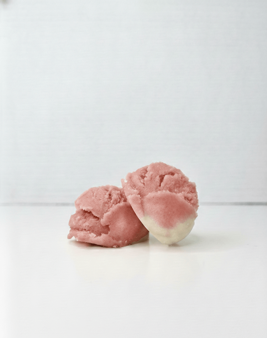 Two white and dusty rose tallow truffles on a white background