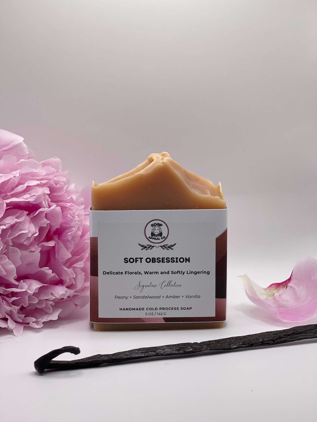 Bar of soap with a label, pink flower, and vanilla bean on a light background