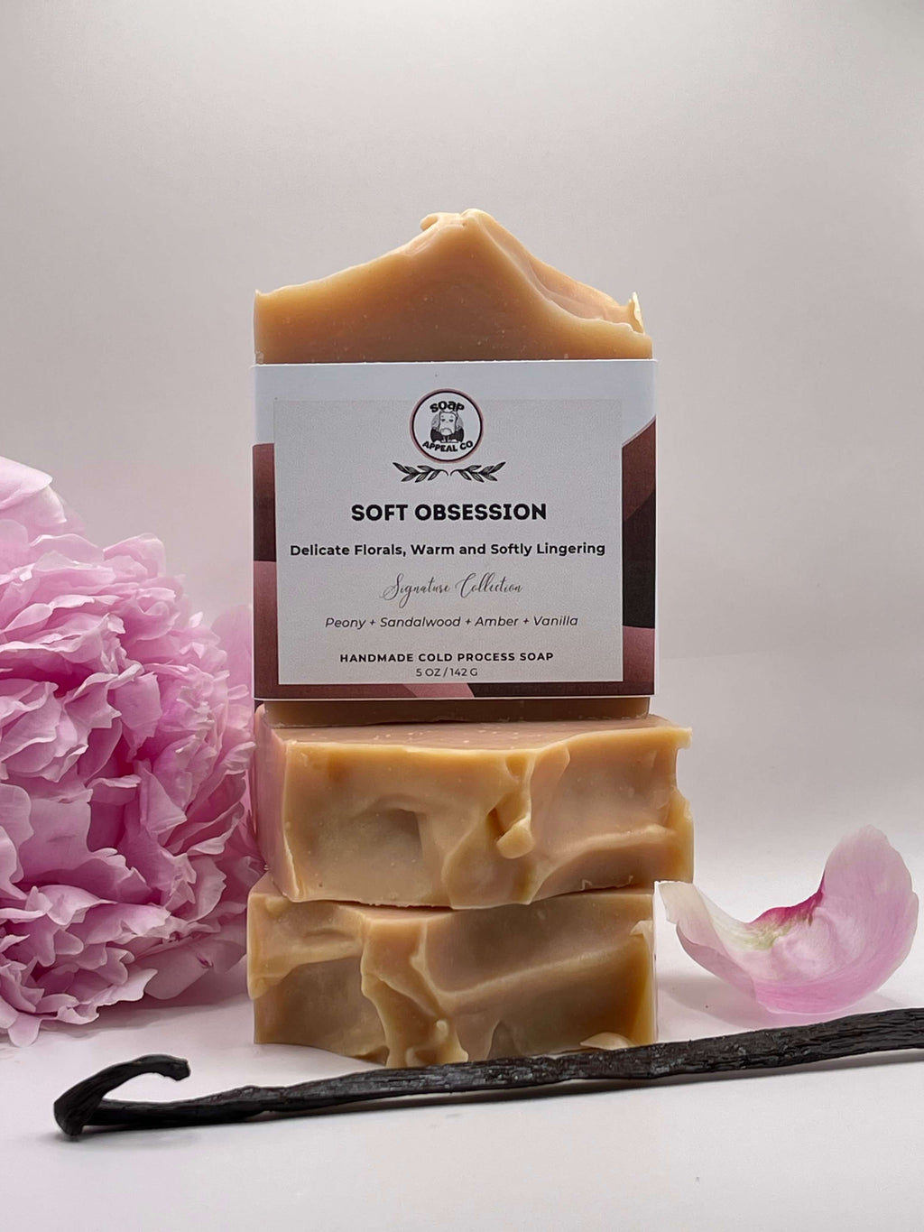 Stack of soap bars with a pink flower and vanilla bean on a light background