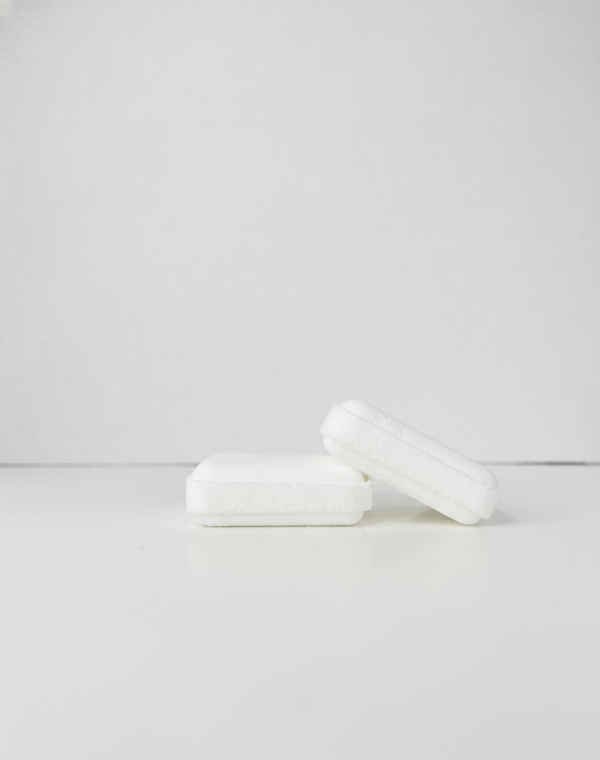 Two white shower steamer squares on a light grey background