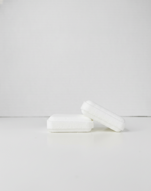 Two white shower steamer squares on a light grey background